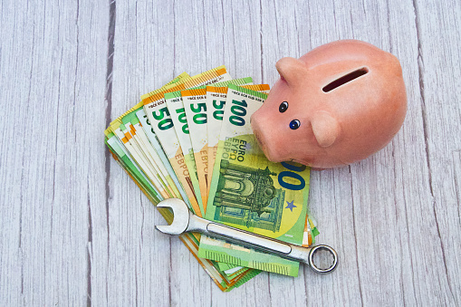 A stack of banknotes with a wrench and piggy bank on a wooden background, horizontal