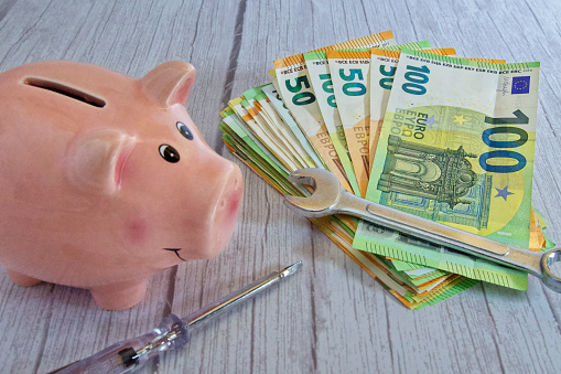A stack of banknotes with a wrench, piggy bank and screwdriver on a wooden background, horizontal