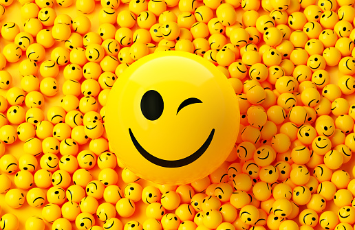 Yellow spheres textured with happy face emoji surrounded by other happy face emojis on yellow background. Horizontal composition.