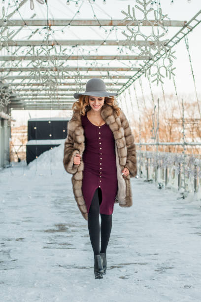 mujer morena sonriente que sale a la calle de la ciudad con sombrero y abrigo de piel - russian culture fashion model hat sensuality fotografías e imágenes de stock