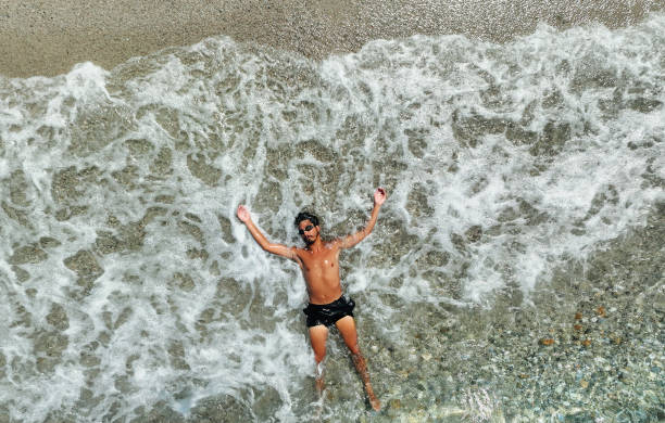 Man wearing swimshorts brushes sand off hands as he stands on beach in Santa Barbara, California.
