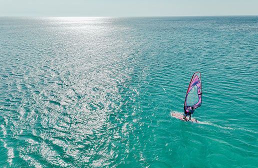 Aerial view photo of a young man windsurfing on the open sea. High angle view. Drone point of view.