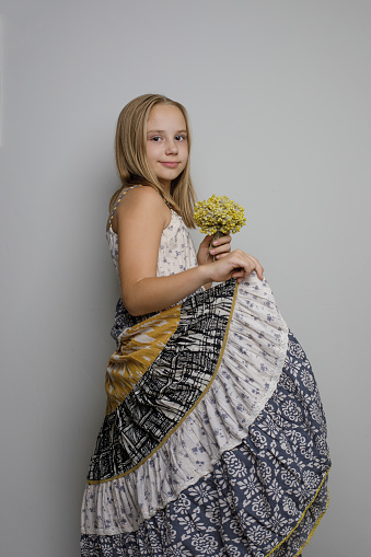 Lovely young girl in long cotton dress with yellow flower in her hand on white background