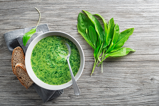 Healthy creamy soup with fresh ramson or wild garlic leaves on wooden background. Healthy spring food concept