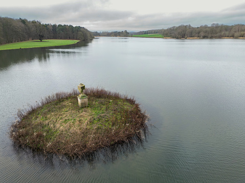 Drone view of a very small, concentric aquatic bird island seen in a large English, freshwater lake. A damaged ceramic ornament can be seen in the middle of the Island.