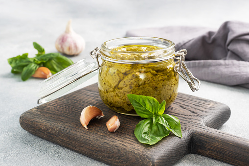Pesto sauce in a glass jar, fresh basil leaves and garlic, copy space