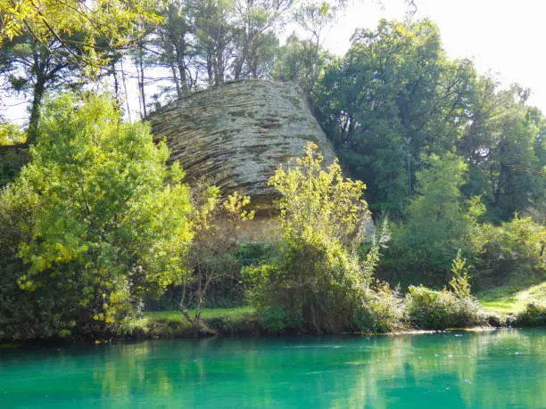 Magnificent photo of a rock of a strange shape at the edge of the Sorgue river in a peaceful and pleasant moment. This photograph was taken at Fontaine de Vaucluse in Provence in France.