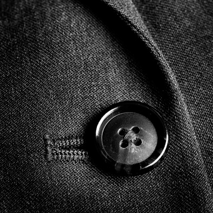 Blurred defocus shot of formal black or dark grey wool suit fabric texture. with button decoration under light and shadow ambient. Ideal for background or wallpaper.