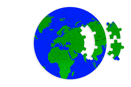 Round puzzle resembling a map showcasing the Eurasian continent in green hues surrounded by blue oceans with two missing pieces set aside. Problems solution related concept.