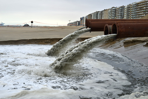 Blankenberge, West-Flanders, Belgium - February 17, 2024: massive seawater coming out of a few rusty pipes from silting sand