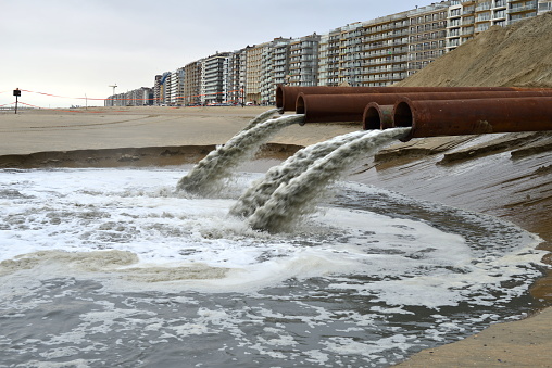 Blankenberge, West-Flanders, Belgium - February 17, 2024: massive seawater coming out of a few rusty pipes from silting sand