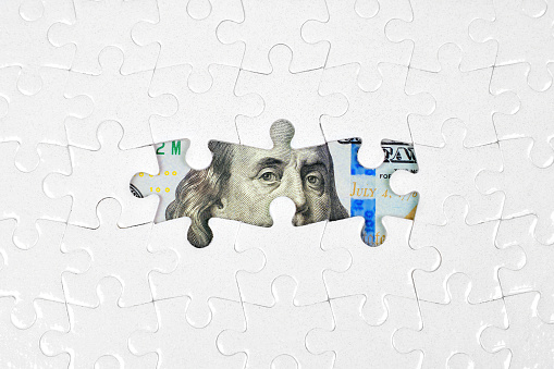 Puzzle background revealing glimpses of one hundred dollar bill elements through the missing pieces. Wealth, strategy and opportunity related concept.