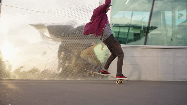 Cool stop on a longboard, an experienced rider does a trick deftly stops the board on the move, camera tracking a man in a helmet on the street near a glass building on a warm summer day