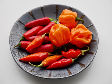 Red hot chilis and Bahamian goat peppers on black ceramic plate.