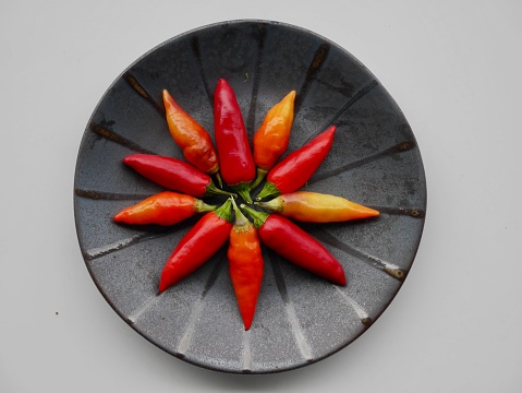 Aerial view of red and orange chilis on black ceramic plate.