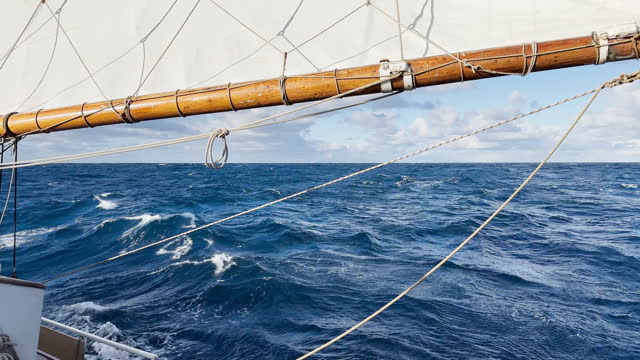 view from a retro style sailing schooner during the passage of the Drake Strait, wooden boat boom, lots of ropes, large waves of the southern ocean in sunny weather