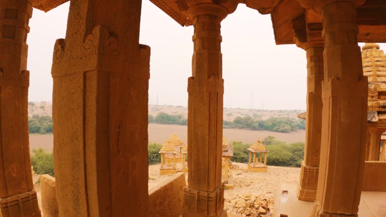 4K shot of royal chhatris made from sandstones in Jaisalmer, Rajasthan, India. Ancient Indian architecture. Exploring heritage sites of India during holidays or vacation. Pillars of cenotaphs.