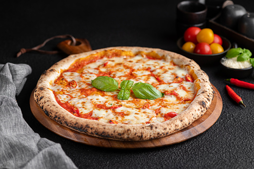 Pizza with basil, tomato, and cheese on wooden platter