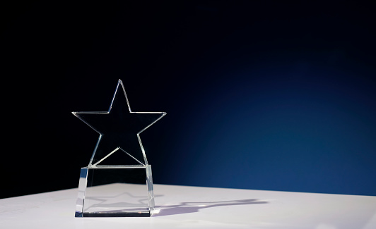 Star-shaped award made of glass on a white table with a spotlight on it