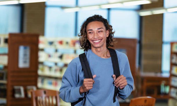 Multiracial teenage boy with backpack in library