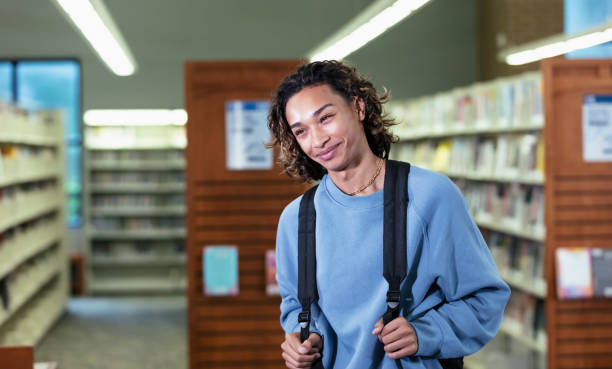 Multiracial teenage boy with backpack in library
