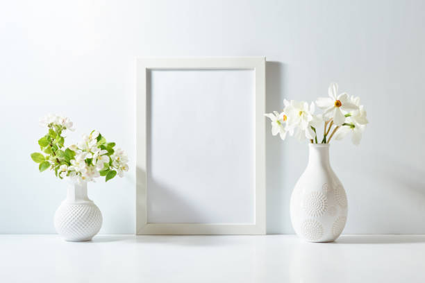 istock Mockup with a white frame and spring flowers in a vase on a white table. Empty poster frame mockup for presentation, design, lettering 2023146618