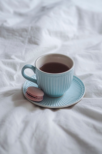 A cup of coffee and a macaron placed on a bed in a cozy setting