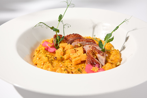 Elegant duck breast with pumpkin risotto in a shadowy white ambiance, perfect for sophisticated culinary presentations.
