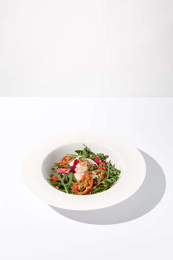 Italian salad with burrata, tomatoes, and arugula, elegantly arranged and garnished with edible flowers.