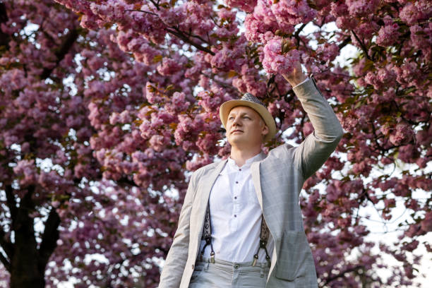 man in a light suit holds onto a blooming sakura branch with his hand