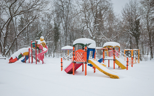 A playground covered in a blanket of snow, with a bright red slide shining against the white backdrop. Snow-covered trees provide a serene and magical atmosphere.