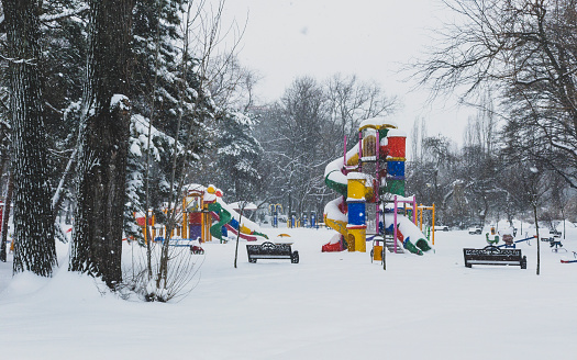 A playground covered in a blanket of snow, with a bright red slide shining against the white backdrop. Snow-covered trees provide a serene and magical atmosphere.