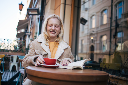 Relaxed young albino woman reading a book at a cafe, drinking coffee.