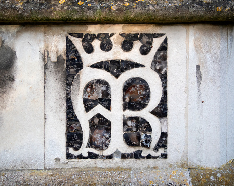 A design made from stone and knapped flint forming the initials A M R - Ave Maria Regina - set into the exterior wall of St Mary the Virgin church in Woodbridge, Suffolk, Eastern England.