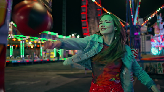 Smiling girl hitting boxing machine at amusement park. Cheerful teenagers having fun celebrating high score in game. Happy friends enjoying funfair evening hang out together. Weekend leisure concept