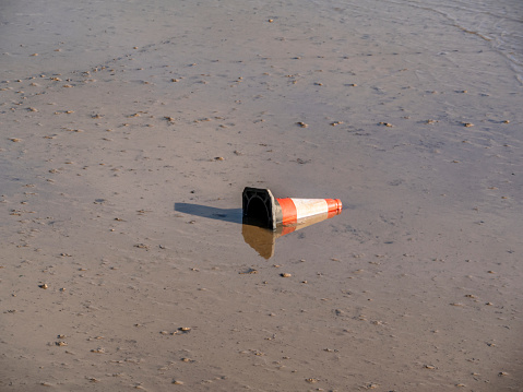 A discarded traffic cone thrown into the muddy river bed of the River Deben in Woodbridge, Suffolk, Eastern England and exposed at low tide.