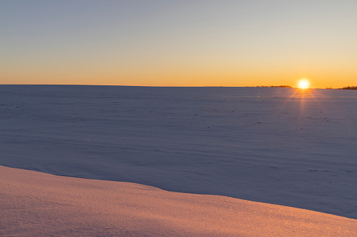 winter field covered with snow at sunset, beautiful multicolored sky at sunset in winter
