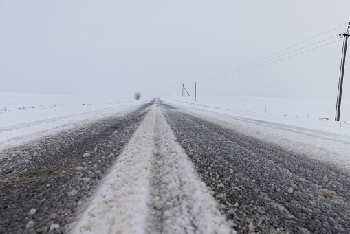 a snow-covered paved road in the winter season in a snowfall, a road during a snowfall, spots from falling snowflakes are visible in the sky