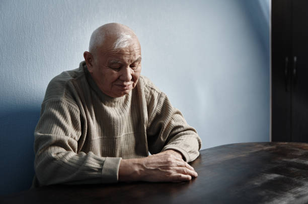 Pensive and thoughtful senior man sitting at the table stock photo