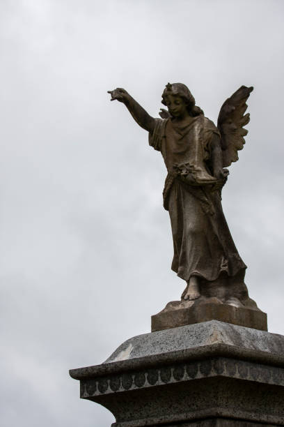 Dublin, Ireland - September 21, 2018: A towering angel statue with one hand raised stands against a dramatic cloudy sky in Glasnevin Cemetery, symbolizing peace and spirituality.