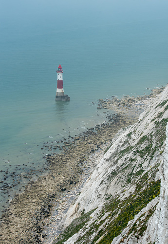 Beachy head lighthouse at the edge of white chalk cliff. Safety warning in the ocean.
