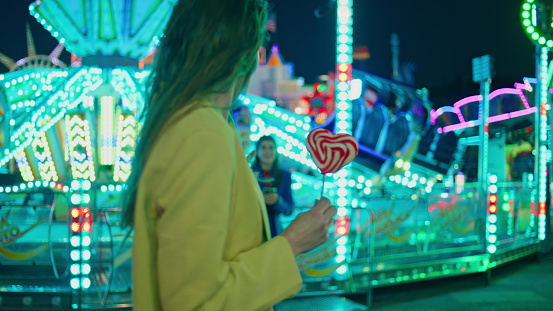 Cheerful friends meeting amusement park at night. Happy smiling girls hugging at neon illuminated carousel. Excited girlfriends sisters embracing have fun together at funfair. Friendship relationship