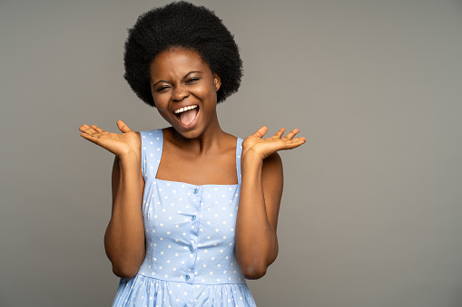Happy thrilled female on grey studio background, laughing have good news lottery prize winning. Overjoyed glad young african american woman with natural curly hair, smiling broadly with opened mouth.