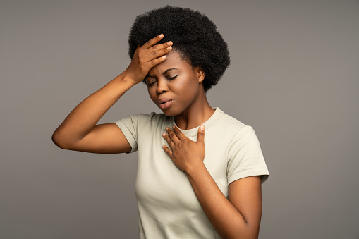 Sick african american woman touch head, having high temperature, migraine. Unwell black female with symptoms of influenza, respiratory virus put hand on breast because of cough, difficult breathing.