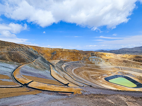 Panoramic view of an open pit mine with a lagoon in the background and sunny weather in Peru.