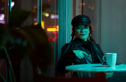 Young woman in glasses and leather hat sitting alone in a café.