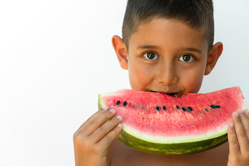 Little boy  eating a slice of watermelon in front of white background with a cute smile.