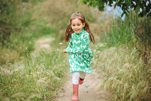 Portrait of cute young girl in white dress picking flowers in field.