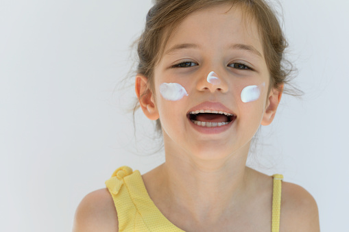 Little girl with sun cream on her face I looking at camera with a toothy smile in front of white background.