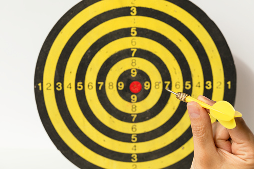 Business person is holding red dart over dart board middle. Achieve success, investment goal and target for business concept.